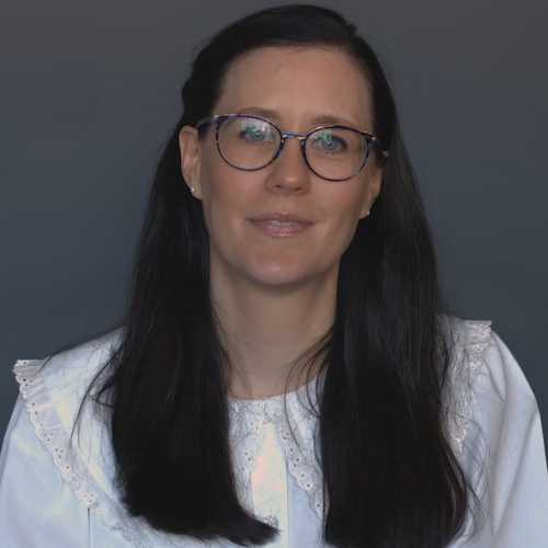 A woman wearing glasses and a white shirt, smiling confidently against a neutral background.