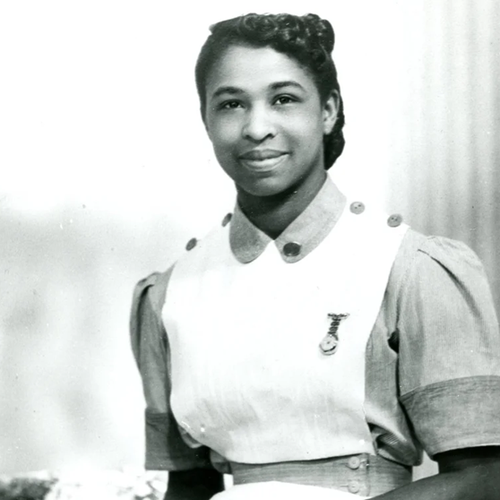 A black and white portrait of Louise Da-Cocodia, smiling for the camera in her smart nurses uniform.