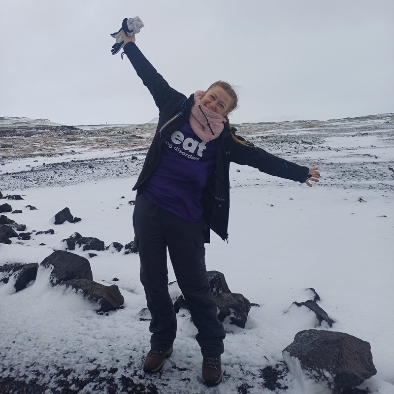Photo of lady wearing a purple Beat t-shirt, arms spread and smiling with a snowy landscape behind her