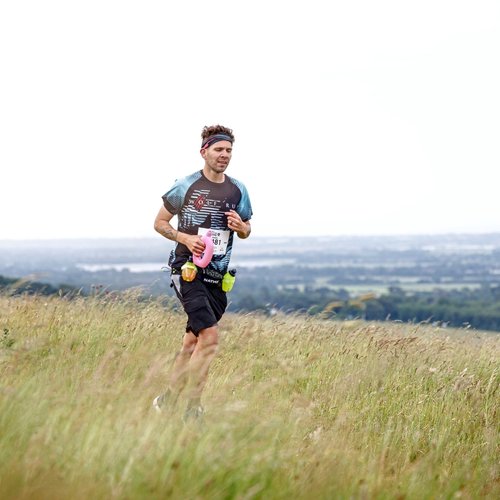 Man running across a field on a hill, with a view of the landscape behind him