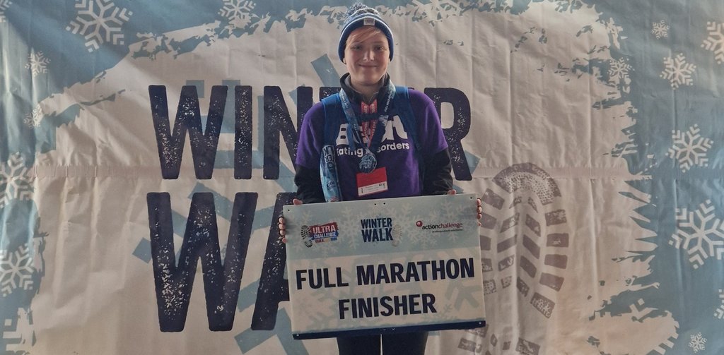 An individual wearing a Beat t-shirt, holding up a sign that says full marathon finisher