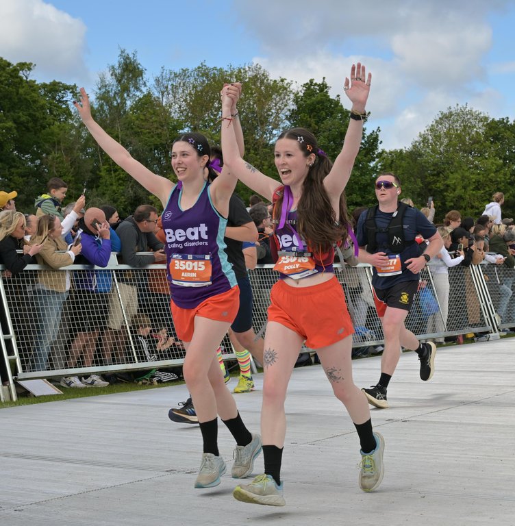 Two ladies wearing Beat vests, running across the finish line, arms raised above their heads