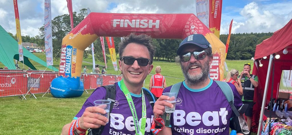 Two men standing next to each other in Beat t-shirts with a finish inflatable behind them